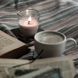 Uploaded photo, square: a lit candle beside a cup of coffee and an open book.
